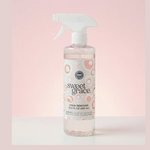Product photo of a Sweet Grace Stain Remover clear spray bottle, 15.2 fl oz, with a white nozzle and a label featuring pink, orange, and white concentric circles, presented against a soft pink gradient background