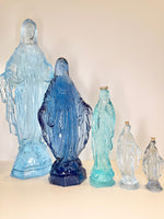 Five blue glass statues of the Virgin Mary in varying sizes arranged in a row