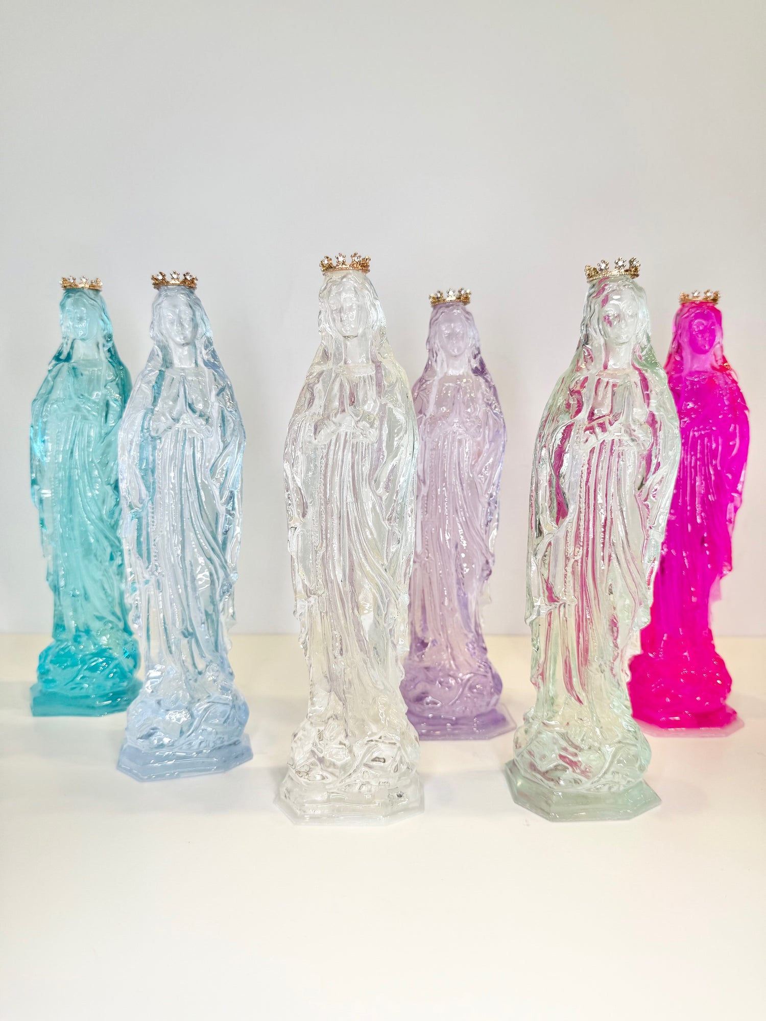 Six translucent resin statues of the Virgin Mary in various colors each wearing a small gold crown