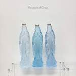 Three blue glass statues of the Virgin Mary with gold crowns on a clear acrylic shelf