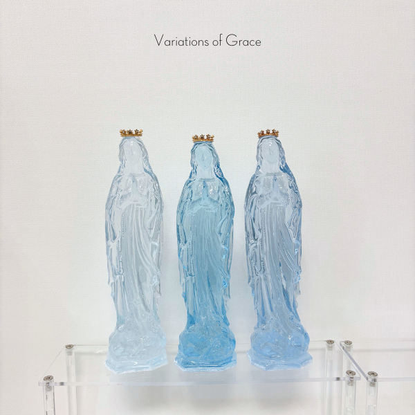 Three blue glass statues of the Virgin Mary with gold crowns on a clear acrylic shelf
