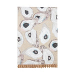 Printed textile art with a repeating pattern of stylized white and gray oyster shells featuring dark centers and subtle pale blue and pink accents on a textured beige background with a fringed bottom edge