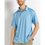 Smiling man wearing a light blue polo shirt patterned with golf carts and flagsticks and khaki pants against a plain white background