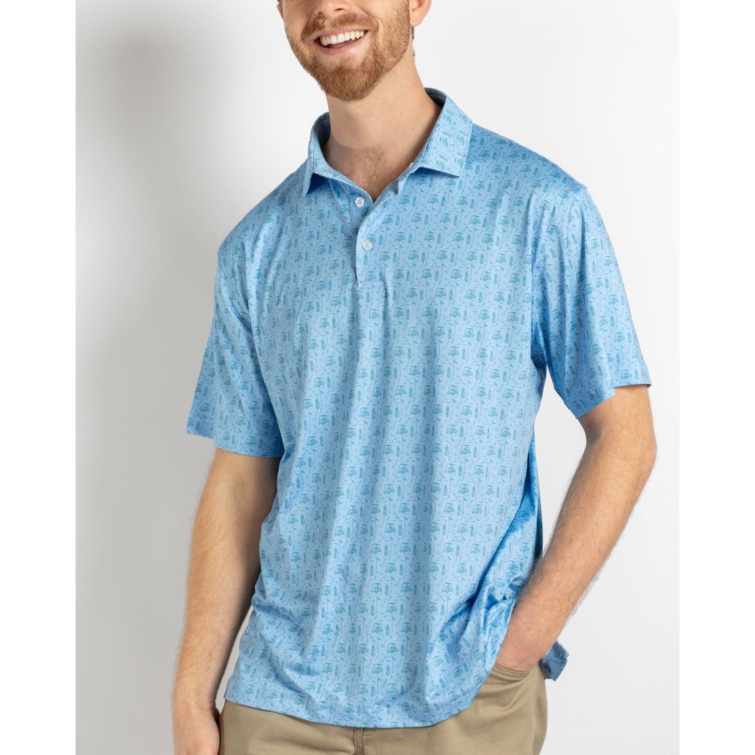 Smiling man wearing a light blue polo shirt patterned with golf carts and flagsticks and khaki pants against a plain white background