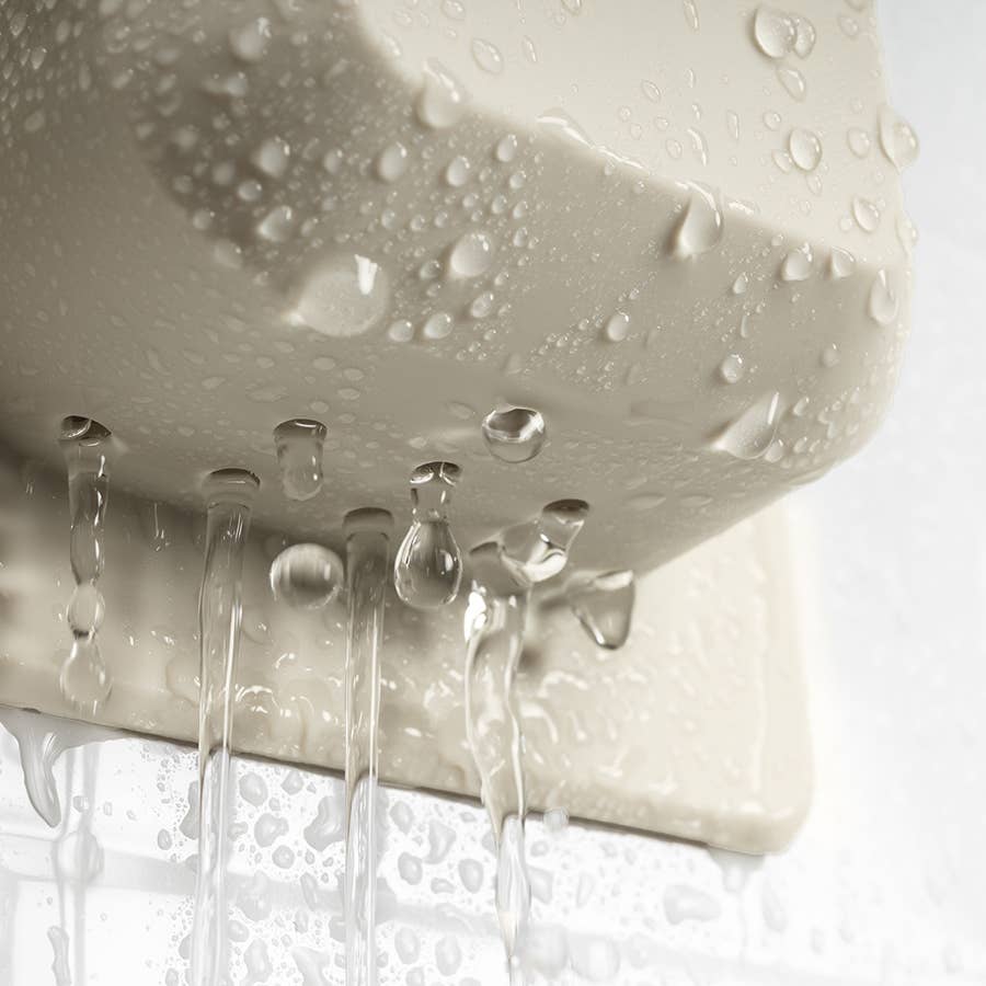A macro photograph captures water cascading from a beige wall-mounted fixture, showcasing translucent spherical droplets and vertical liquid streams against a soft-focus textured surface