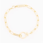 Michelle McDowell gold bracelet featuring a paperclip chain, an O-ring toggle clasp with a female symbol, and a rectangular brand tag