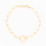 Gold bracelet by Michelle McDowell featuring a paperclip chain a prominent circular toggle clasp with a small female symbol charm and an engraved Michelle McDowell tag