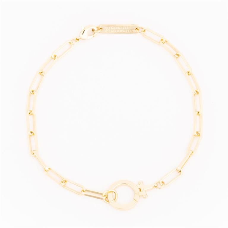 Michelle McDowell gold jewelry, a paperclip chain bracelet arranged in a circle on a white background, featuring elongated rectangular links and a round toggle clasp with an engraved brand tag