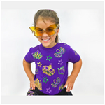 Photograph of a smiling young girl in a studio wearing yellow glitter butterfly sunglasses and a purple t-shirt with gold green and purple sequined Mardi Gras crowns masks and stars