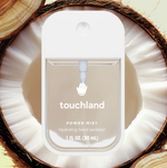 Touchland Power Mist hydrating hand sanitizer spray bottle resting on a halved coconut