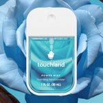 Touchland Power Mist hydrating hand sanitizer spray bottle in front of a blue rose