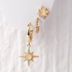 A set of three gold earrings displayed on white featuring a large hoop with a starburst charm and pale yellow stone, a small beaded hoop, and a starburst stud with a central yellow cabochon