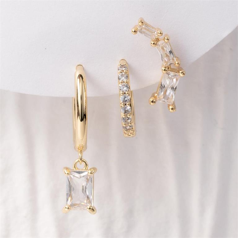 A close-up of three gold-plated earrings on a white background, featuring a hoop with a dangling rectangular cubic zirconia, a pave-set mini hoop, and a curved ear climber with three baguette-cut cubic zirconia