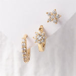 Gold-toned earring set showcasing a sparkling star stud, a floral cluster huggie, and a pavé hoop, all featuring clear diamond-like stones on a white background