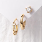 Photograph of a three-piece gold earring set featuring a round clear diamond stud, a plain chunky gold hoop, and a gold hoop with three marquise-cut clear gemstones all displayed on a white card