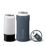 Studio product photography of a white aluminum can next to a gray Brumate Hopsulator TRIO insulated can cooler holding a can and a separate clear Brumate lid with a gray flip-top all on a black reflective background