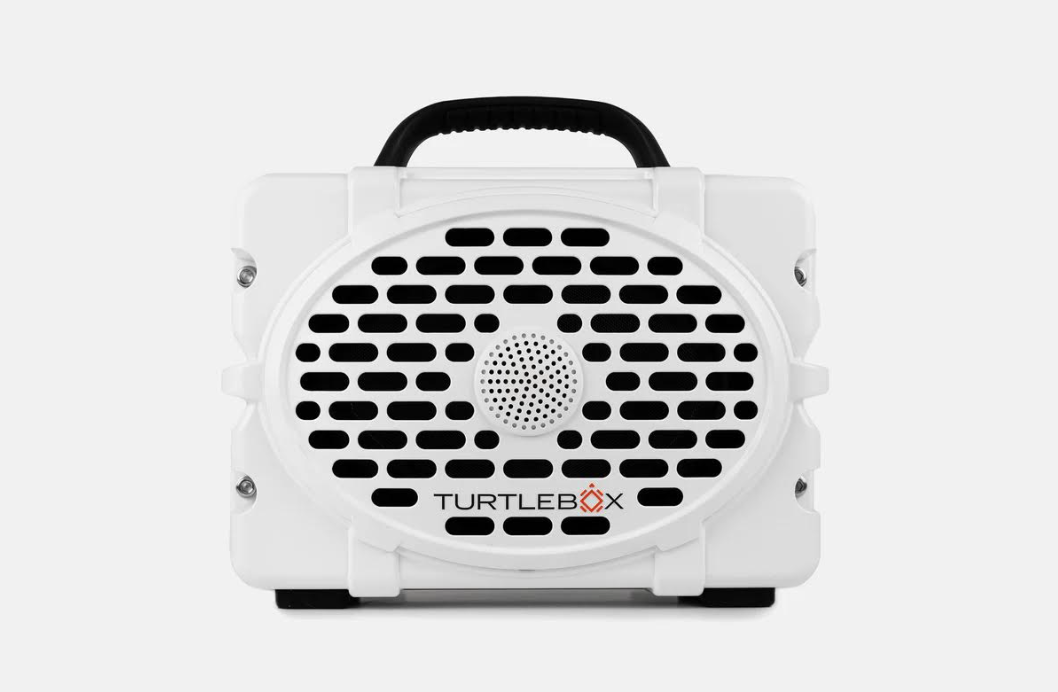 Product photography of a white Turtlebox rugged portable speaker featuring a black top handle, a distinctive oval grille with horizontal slots, and the Turtlebox logo with a red X on a clean white background