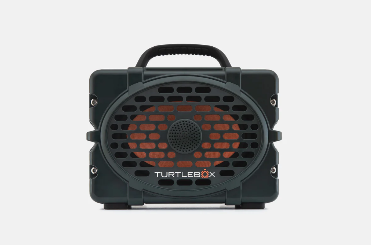 Digital photograph of a Turtlebox speaker, a rugged dark green portable speaker on a plain white studio background featuring an orange speaker cone visible behind an oval black protective grille, a sturdy black top handle, and the white TURTLEBOX logo prominently displayed