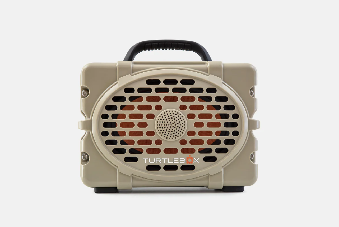 A tan rugged TURTLEBOX portable speaker featuring a black top handle and an orange speaker grille on a white background
