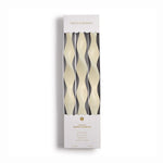 Two's Company product image of three 12-inch creamy white plant-based wax taper candles featuring a unique wavy sculptural design in their white packaging highlighted as fragrance-free and dripless