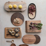 A flat lay arrangement of various natural wooden serving boards and trays featuring yellow plums red grapes ginger root fresh beetroots with green tops and poppy seed bagels on a textured light grey surface