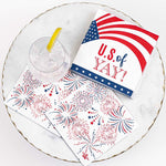 Photograph of patriotic paper napkins and a glass of ice water on a gold-rimmed marble plate featuring the American flag with the phrase U.S. of YAY! alongside red and blue firework patterns and a bright yellow lemon wedge