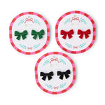 Studio photograph of three pairs of velvet bow earrings in green, red, and black, each displayed on a round 2 Chic branded card with a pink and red striped border and festive leaf designs