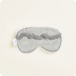 Product photo of a Warmies gray plush sleep mask on a light studio background featuring a ruffled elastic strap, white fluffy trim, and a visible Warmies brand tag