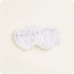 A light purple and white fluffy faux fur eye mask with a small "Warmies" brand tag visible on the right on a plain light background