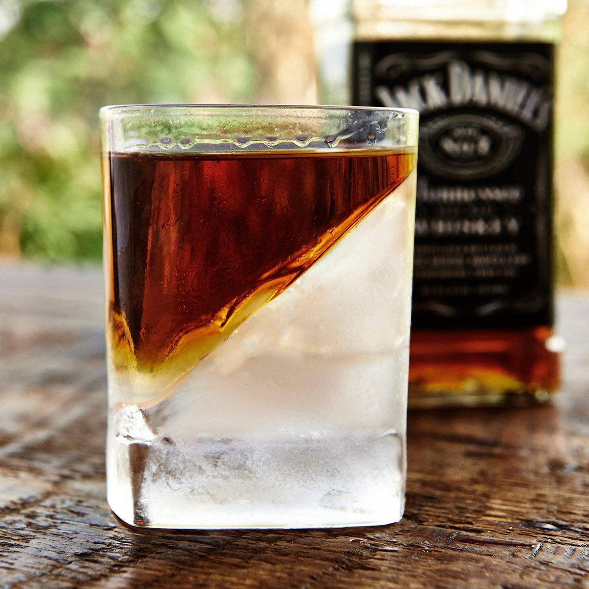 Glass of whiskey with a diagonal ice cube and a Jack Daniels bottle in the background