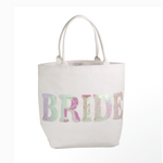 White canvas tote bag featuring the word BRIDE spelled out in shimmering iridescent sequins that display pink green and white hues with two sturdy top handles