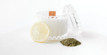 Glass candle jar with wooden wick next to a lemon slice and a small pile of dried herbs