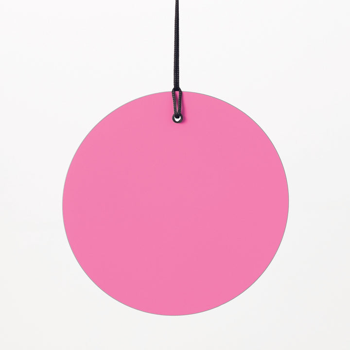 Photograph of a vibrant pink circular disc suspended by a black cord and small black metal loop against a plain white background