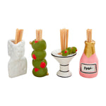 A set of four ceramic toothpick holders including a white Swiss cheese block, a stack of three green olives with red pimentos, a martini glass with olives, and a pink Rosé champagne bottle with a gold foil top, all filled with wooden toothpicks on a white background
