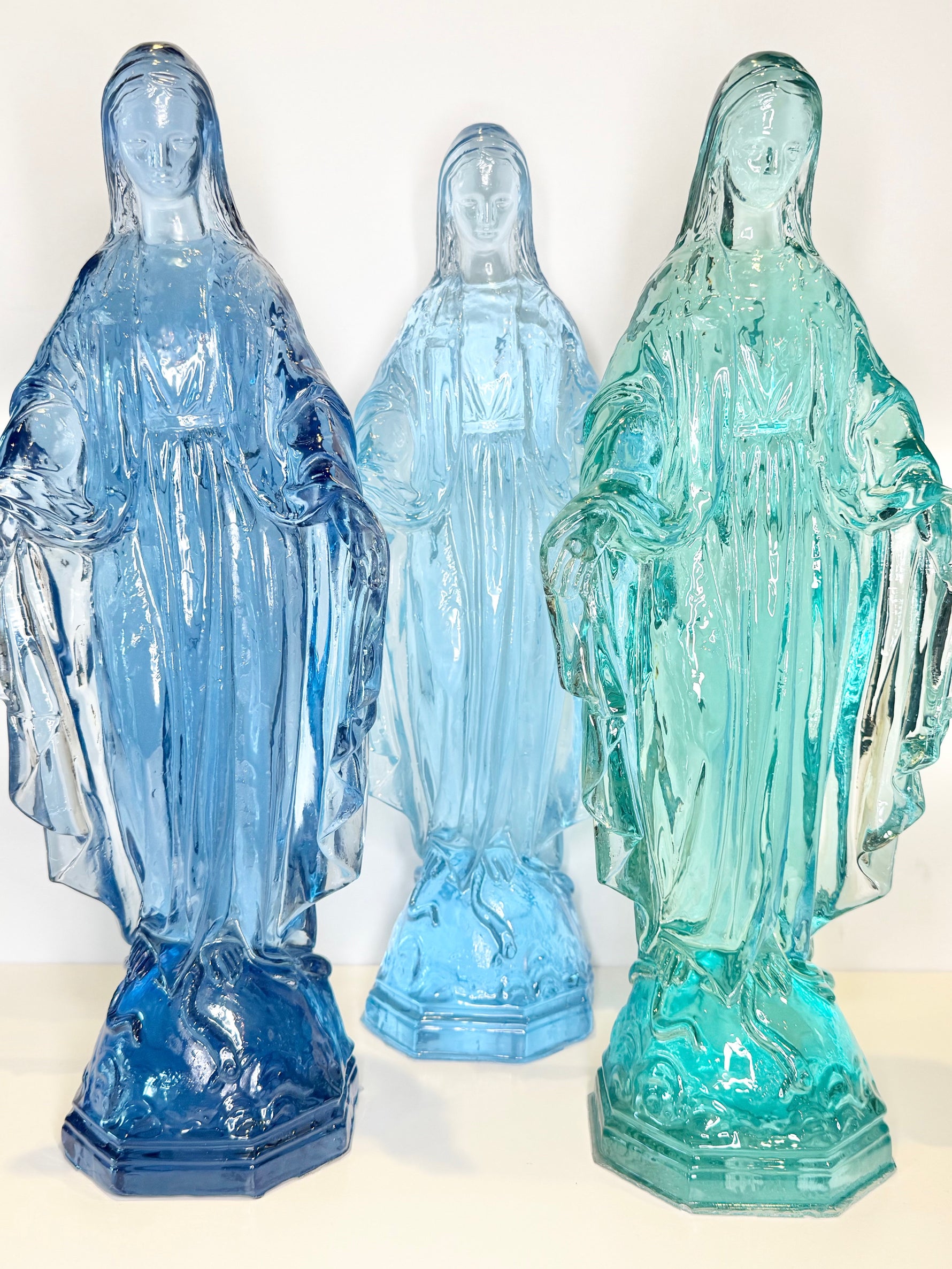 Three glass statues of the Virgin Mary in blue and green shades