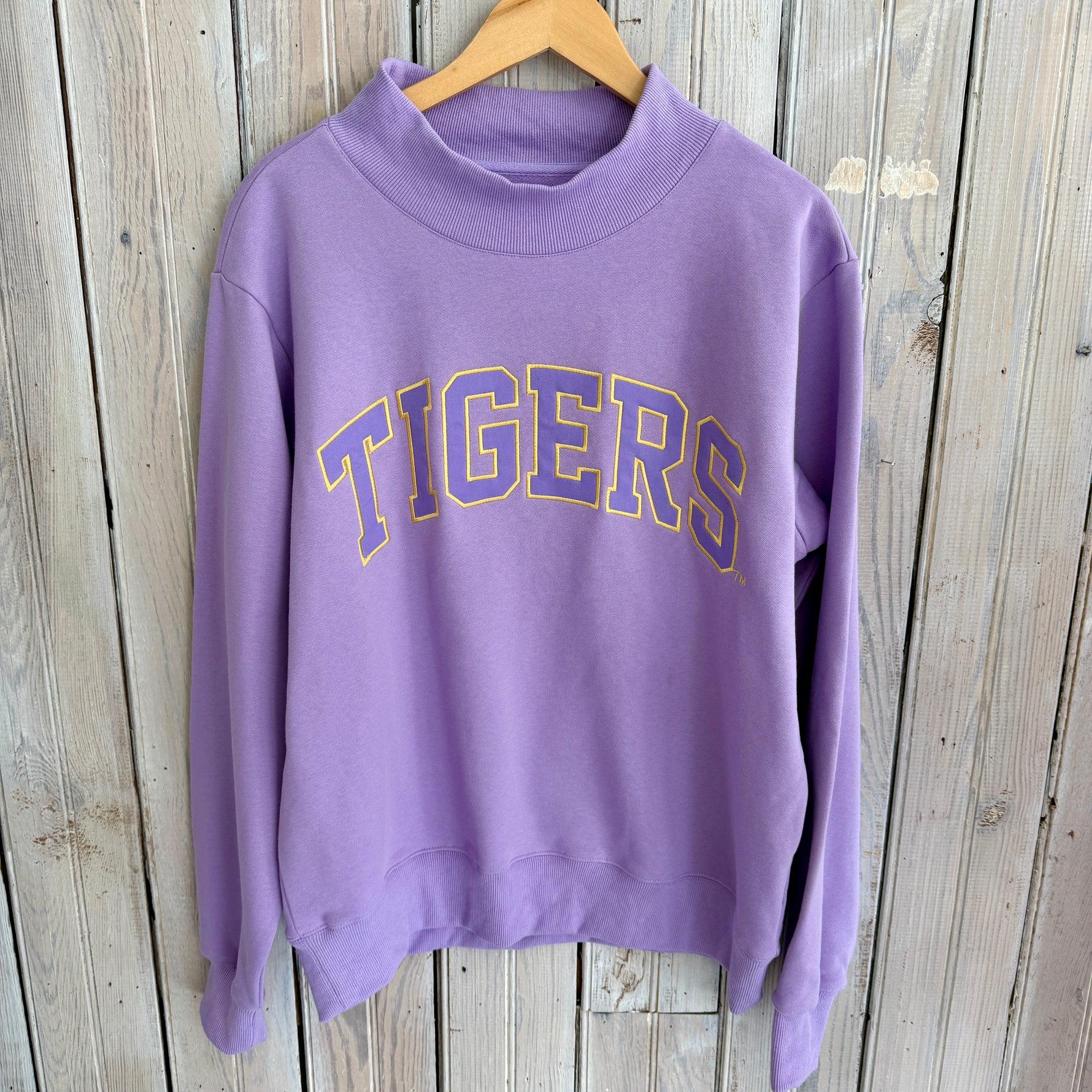 Purple sweatshirt with 'TIGERS' text on a wooden background