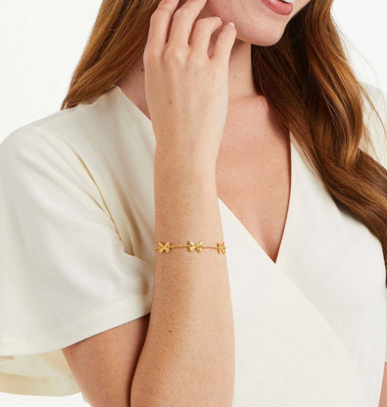 Gold chain bracelet with three small butterfly charms worn on a wrist