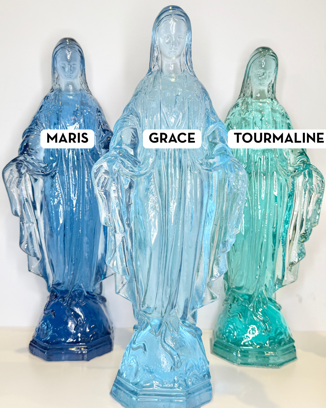 Three glass statues of the Virgin Mary in blue and green shades labeled Maris Grace and Tourmaline