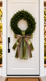 White front door with a boxwood wreath and an olive green ribbon bow with pink woven trim