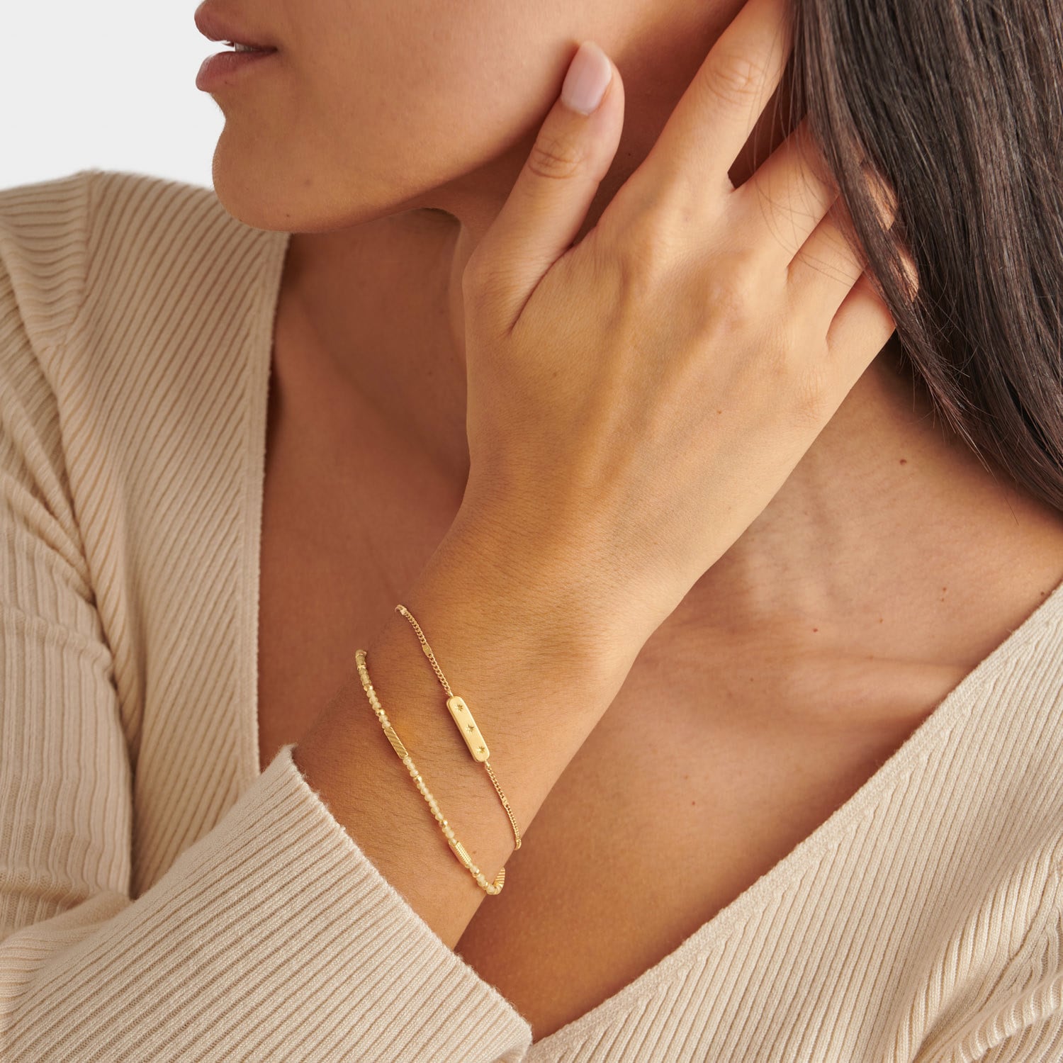 Two gold bracelets on a wrist featuring a beaded chain and a bar charm with star details