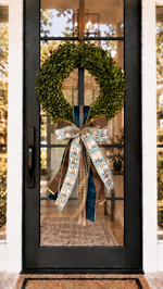 Green boxwood wreath with a decorative blue and brown pumpkin print bow hanging on a black glass door