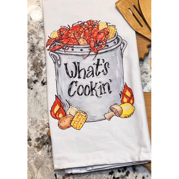 Kitchen towel with crawfish and corn design and 'What's Cookin'' text on a marble countertop.