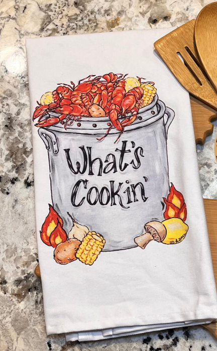 Kitchen towel with crawfish and corn design and 'What's Cookin'' text on a marble countertop.
