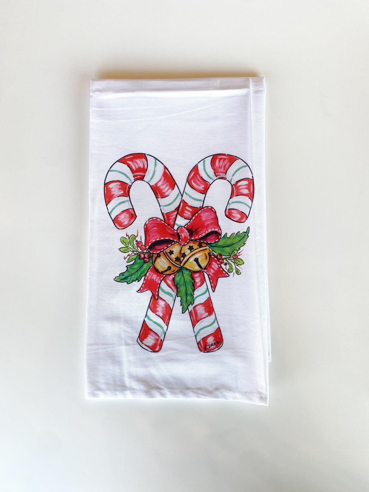 White towel printed with two crossed candy canes tied with a red bow, holly and gold bells