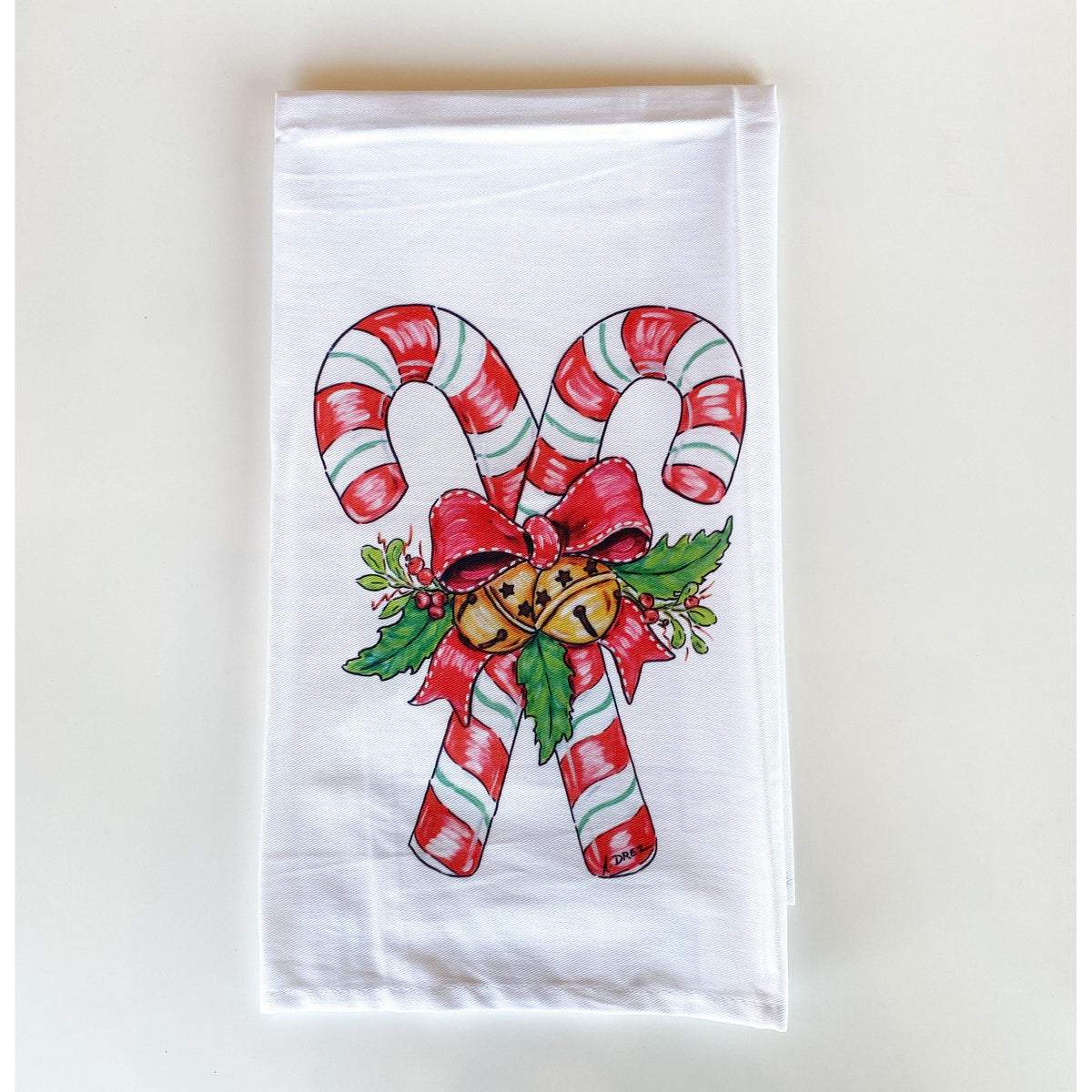White towel printed with two crossed candy canes tied with a red bow, holly and gold bells