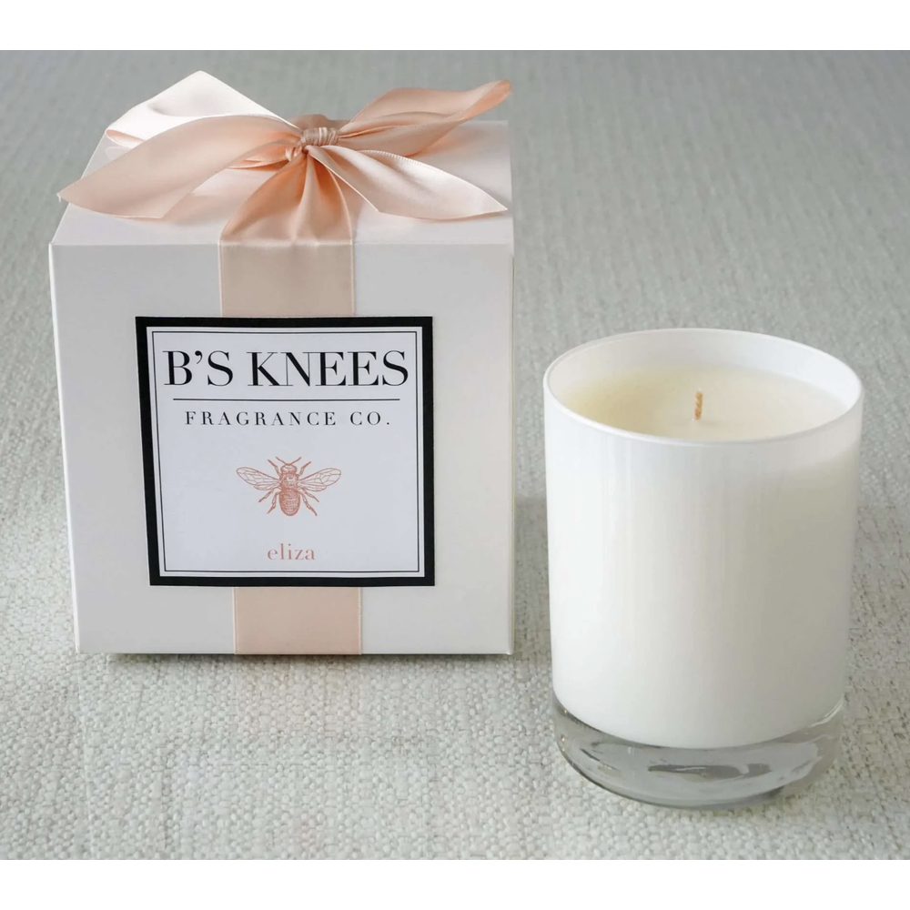 White candle in glass jar next to a gift box with a pink ribbon and Bs Knees Fragrance Co label
