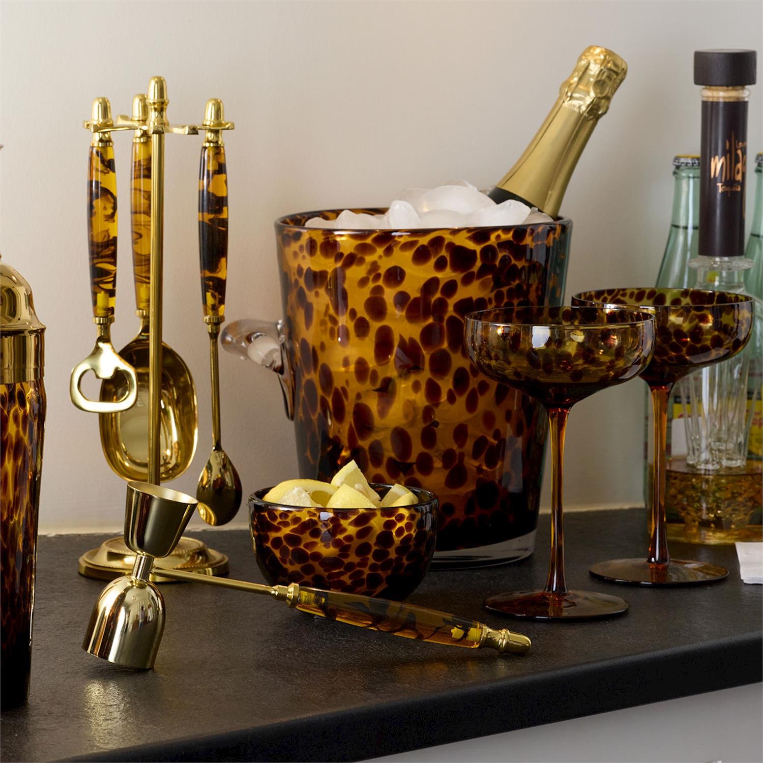 Tortoiseshell pattern barware set including ice bucket, cocktail glasses, jigger, and bar tools on a counter