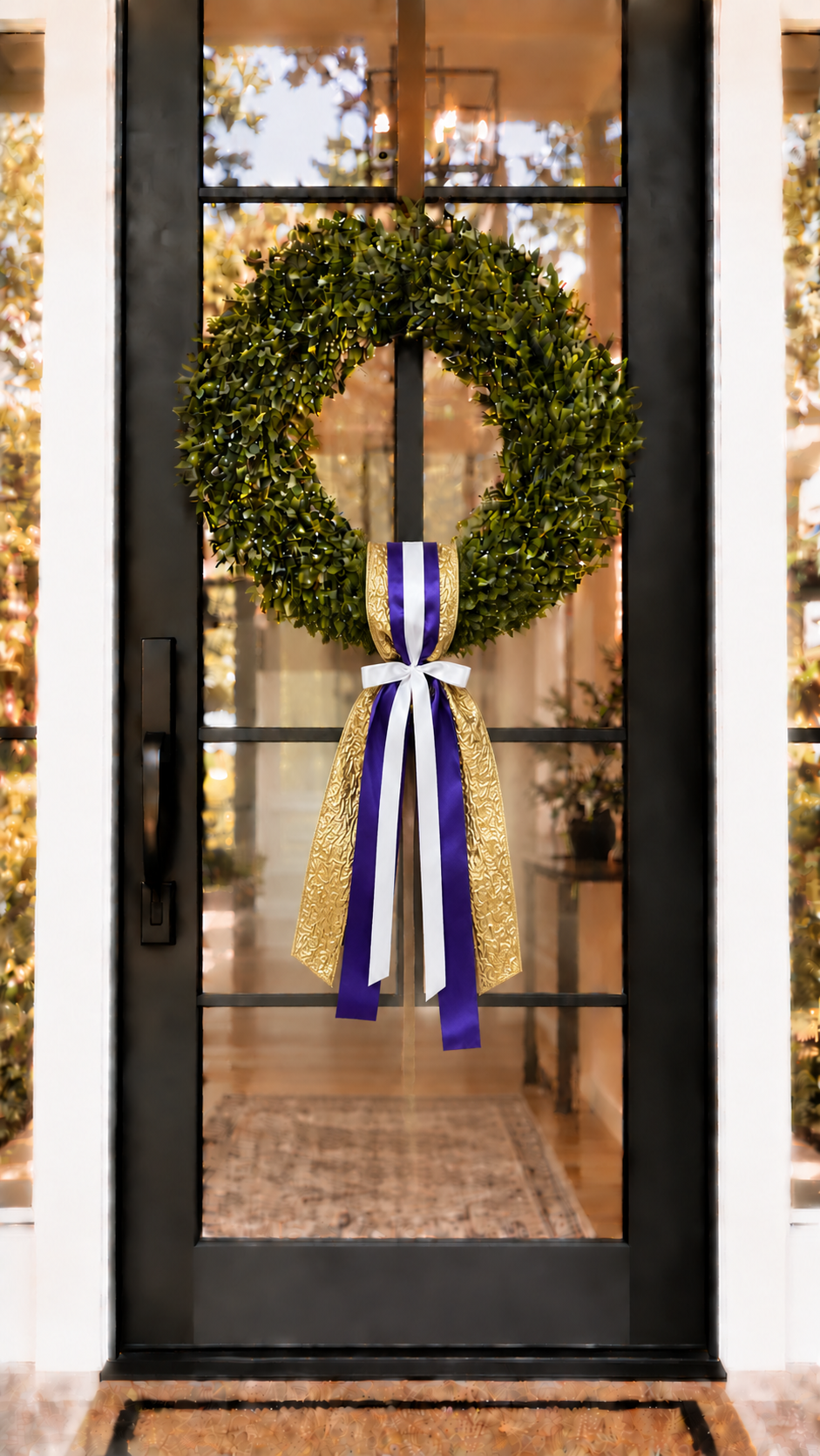 Green boxwood wreath with purple white and gold ribbon on a black front door
