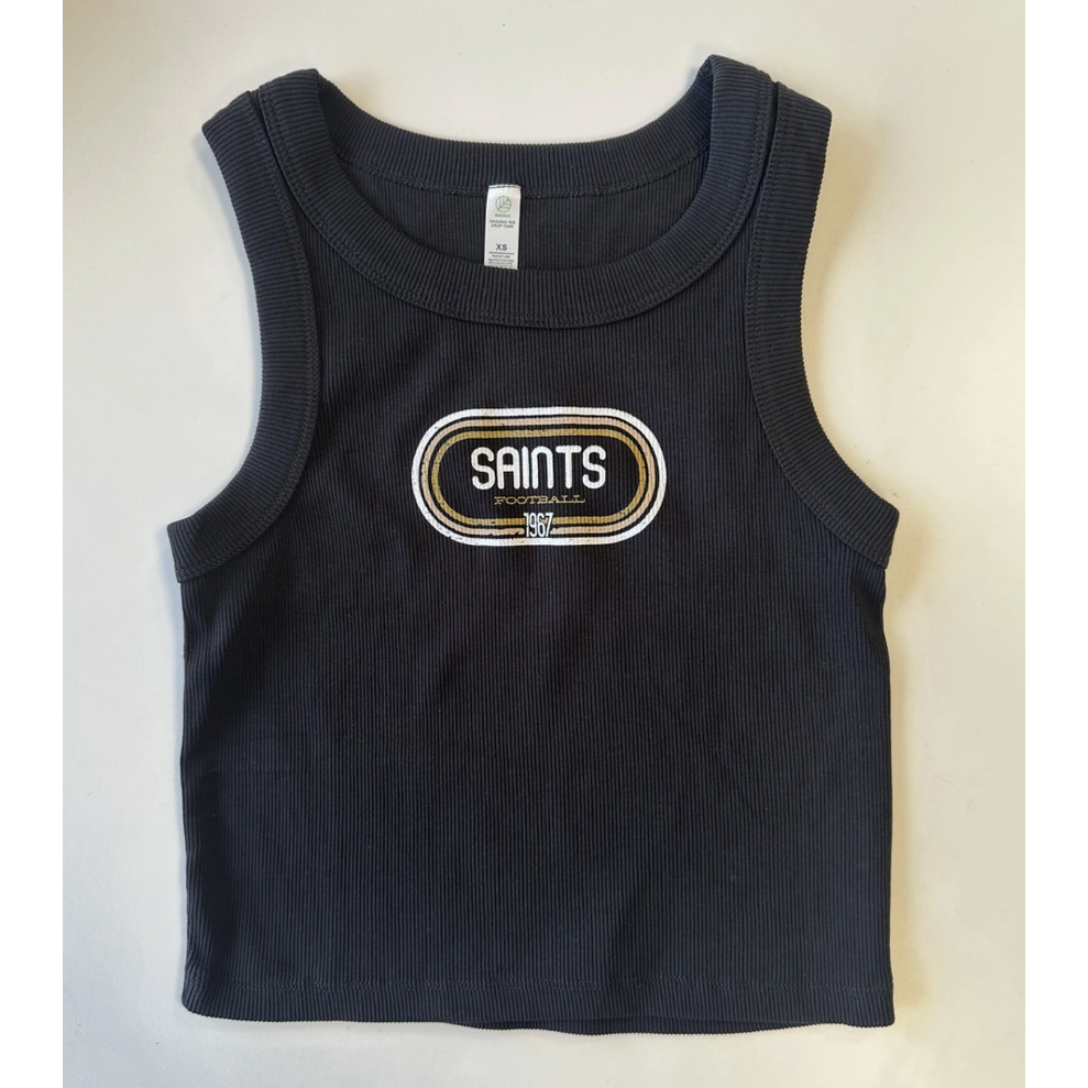 Photograph of a black New Orleans Saints ribbed crop tank top featuring a retro oval graphic with the text SAINTS FOOTBALL 1967 and gold and white concentric borders on a white background