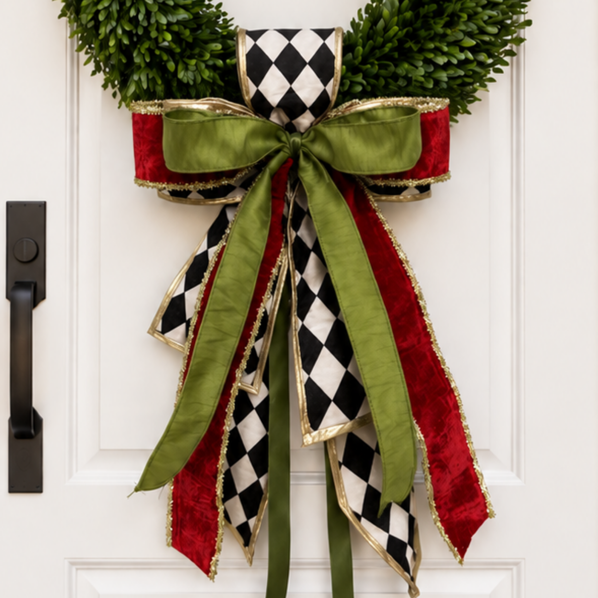Bow of black and white harlequin, olive green and red velvet ribbons with gold edges on a boxwood wreath